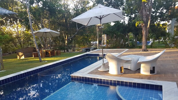 A swimming pool with tiled edges, surrounded by outdoor seating and umbrellas. - Home. Spectacular, 5 Suites, High Standard, ITACIMIRIM. CONDITION QUINTA DAS LAGOAS.  (Camaçari)