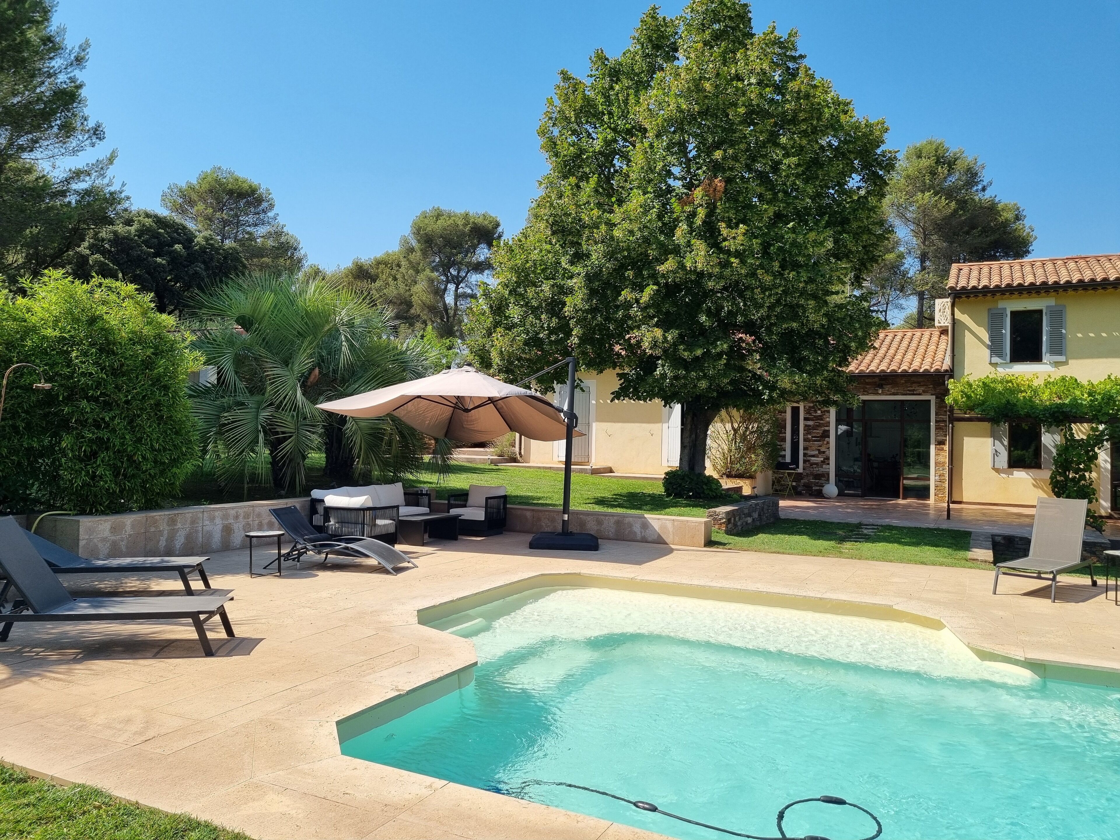 A swimming pool with lounge chairs and a table, surrounded by greenery and a house.