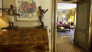 Een kamer met een houten dressoir, een schilderij en uitzicht op een andere kamer met een tafel en stoelen.