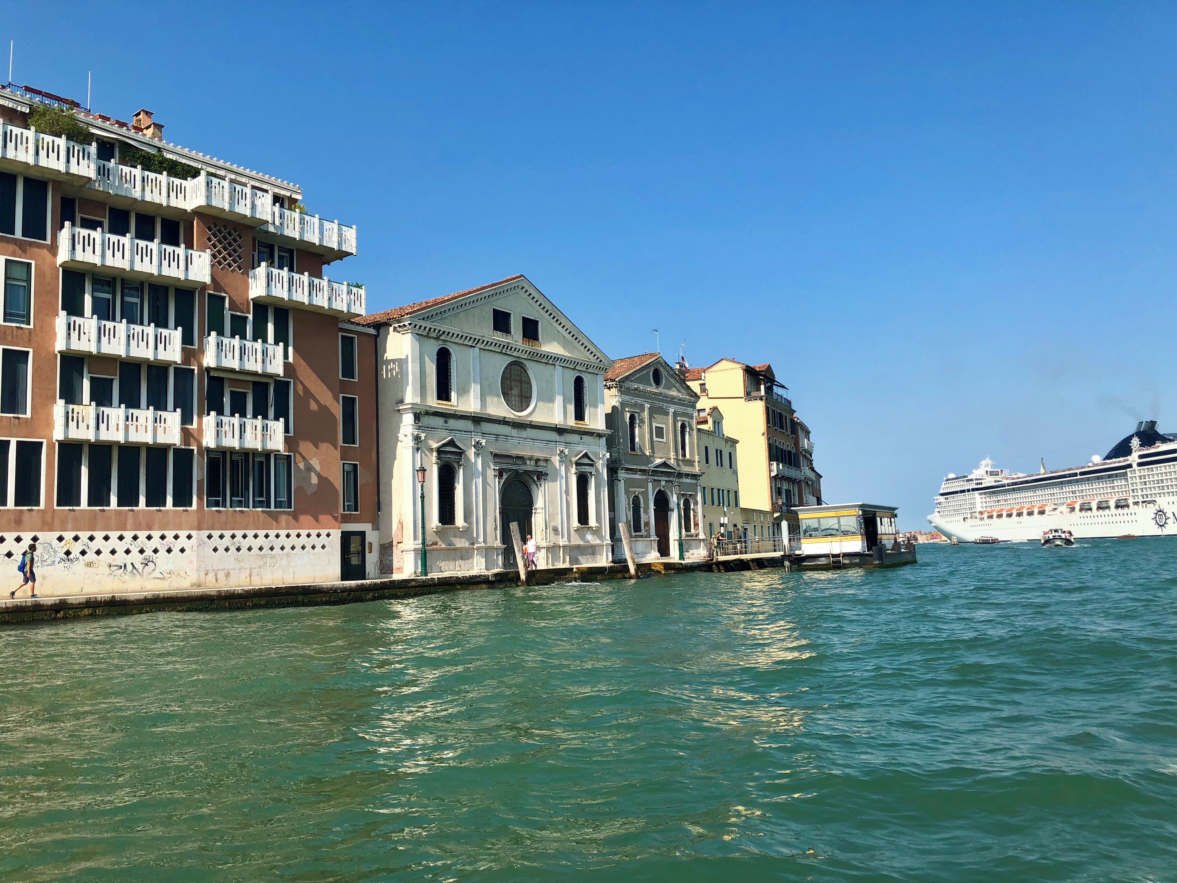 A waterfront building with multiple balconies and a large cruise ship in the background.
