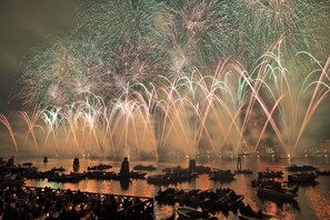 A nighttime scene with fireworks over a body of water, boats, and people on the shore. - Zattere Luxury Apartment (Venezia)