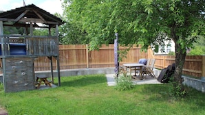 Un cortile con una struttura giochi in legno, un tavolo da picnic e un barbecue.