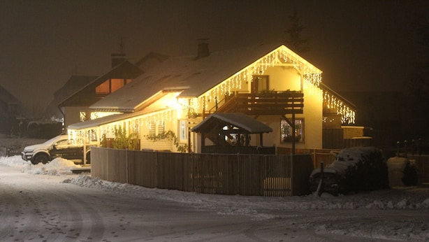 Una strada innevata che conduce a un edificio con una recinzione di legno e un'area esterna coperta con posti a sedere.