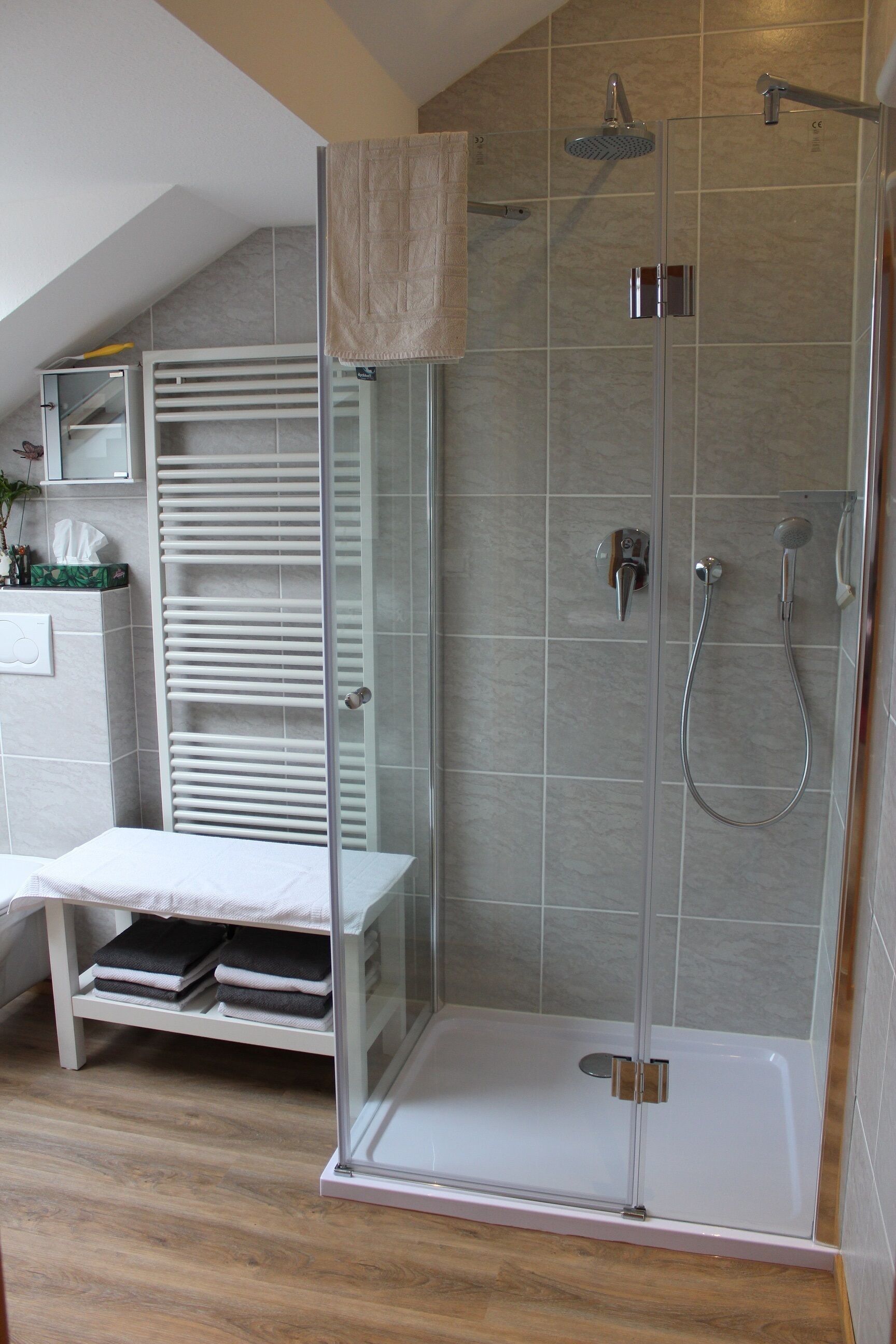A modern bathroom with a glass-enclosed shower, a white towel rack, and a shelf with folded towels.