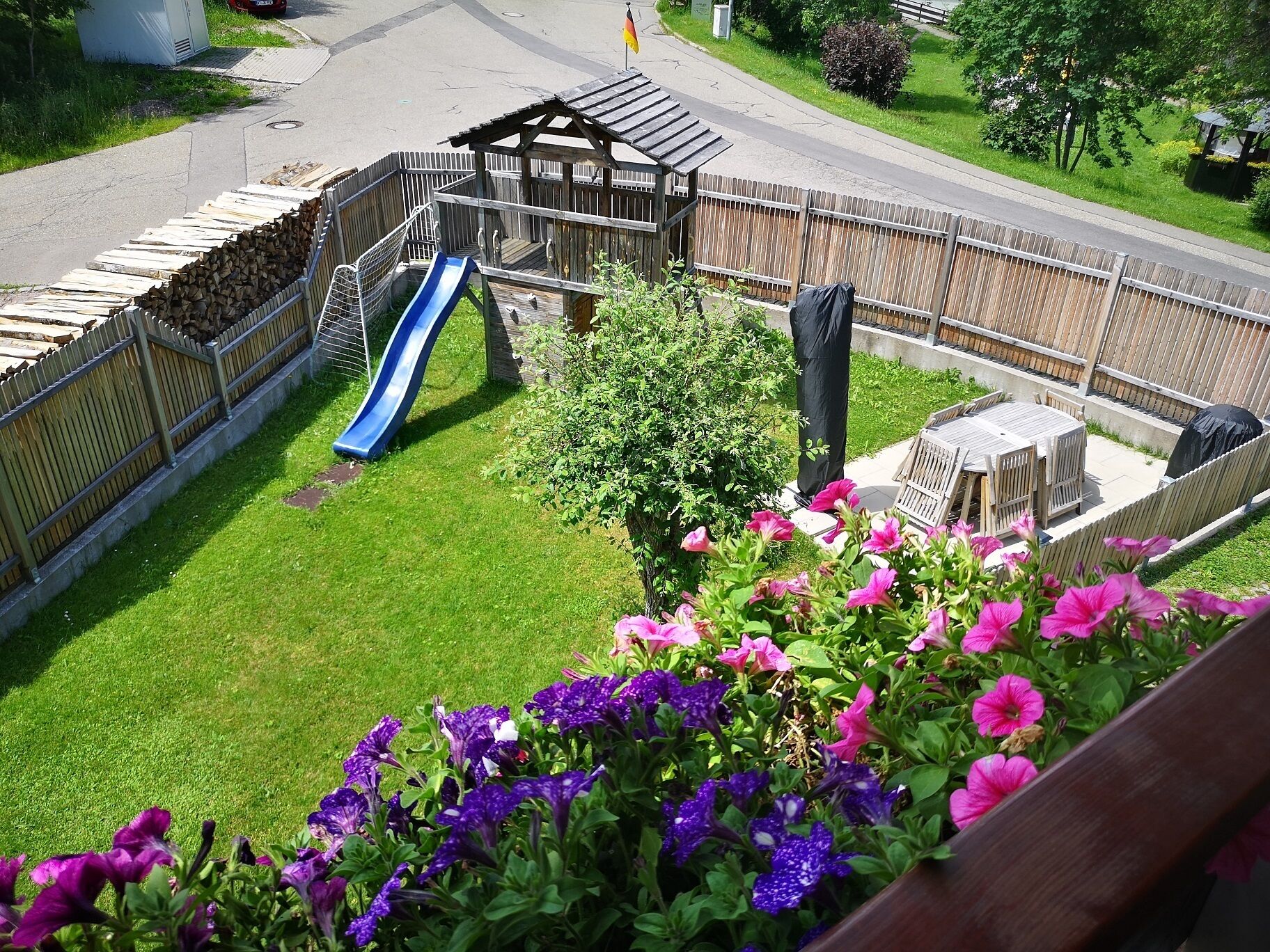 Une cour arrière clôturée avec une structure de jeu en bois, un toboggan et un espace barbecue.