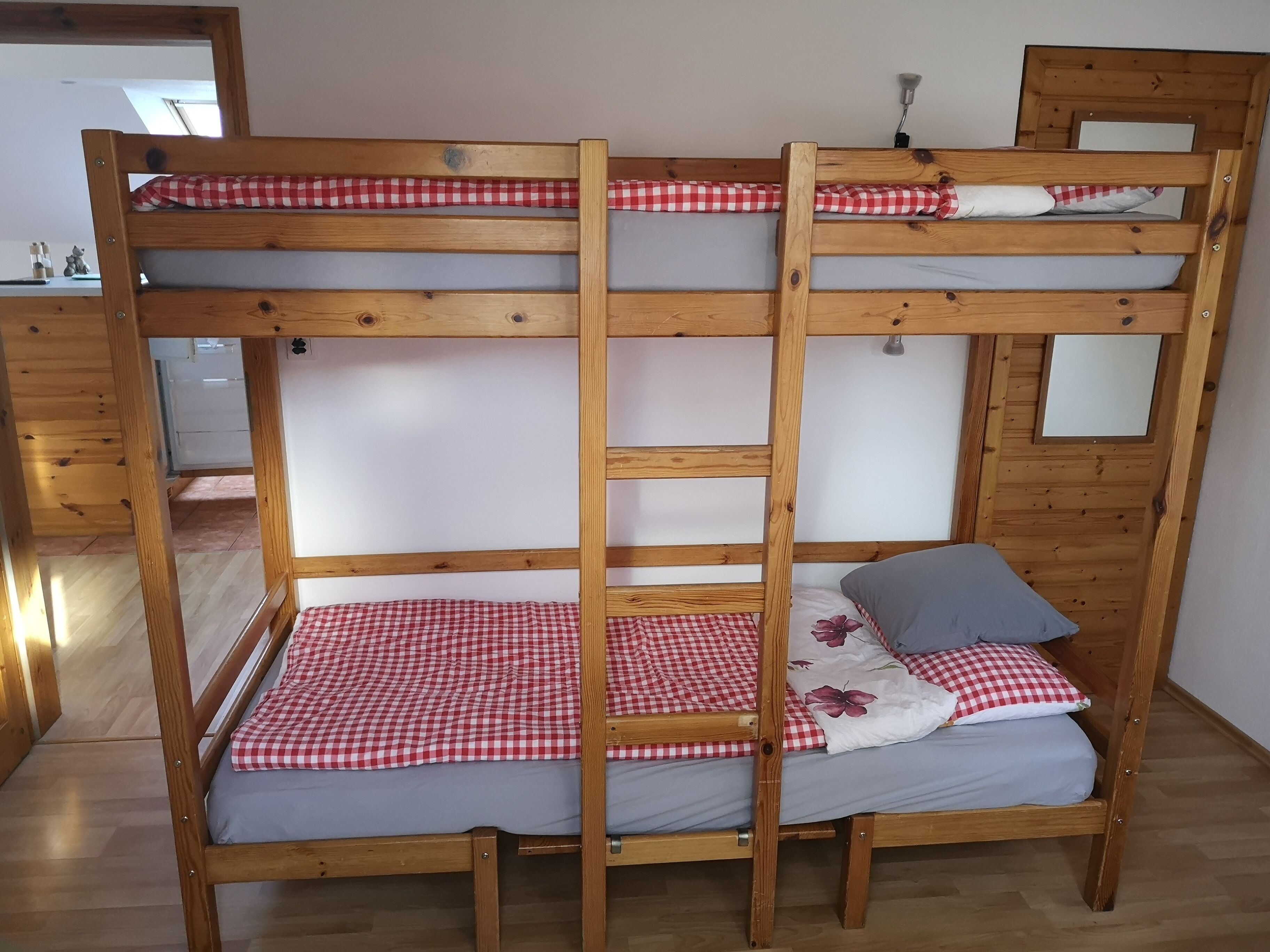 Ein Etagenbett mit rot-weiß karierter Bettwäsche, einem Holzrahmen und einem Spiegel im oberen Bett.