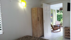 Ett rum med en säng, en garderob i trä, en dörr som leder ut till ett utomhusområde med ett bord och stolar samt en väggmonterad lampa.