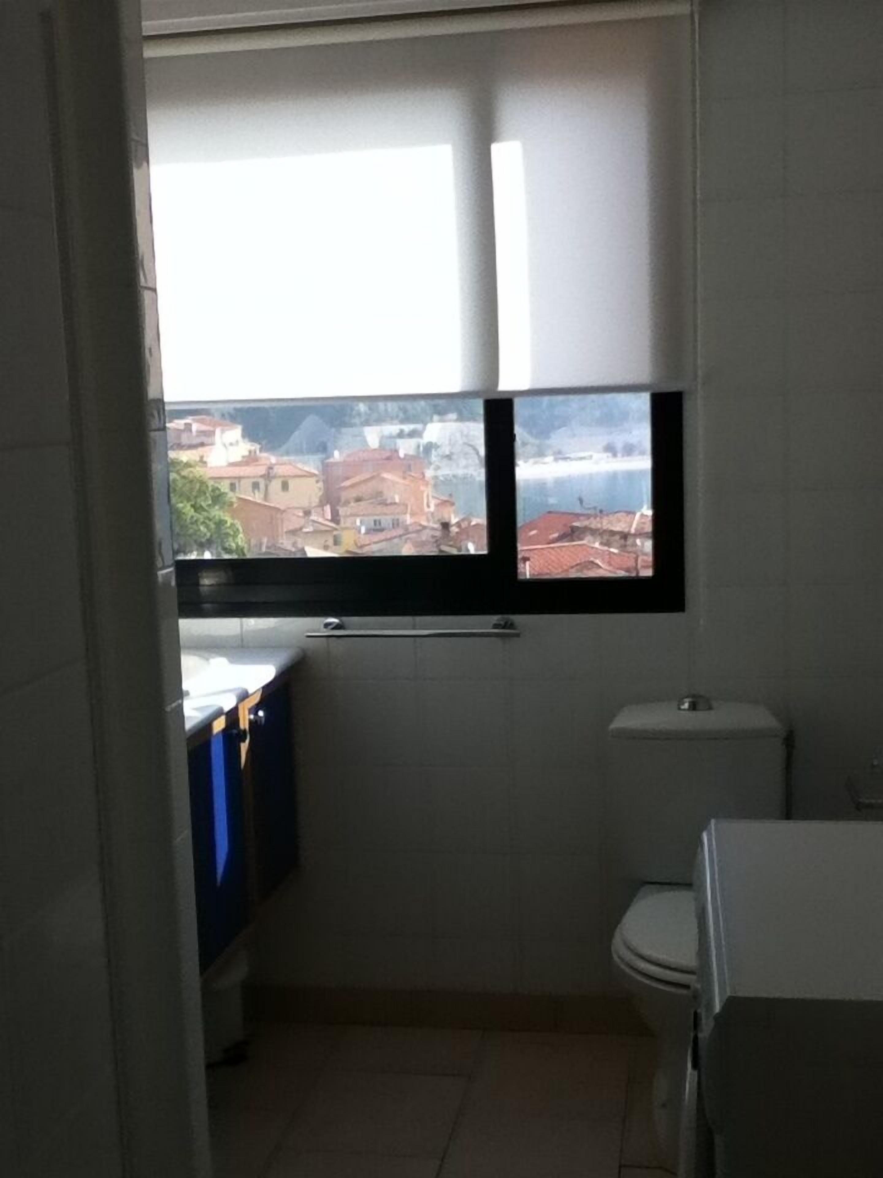 Ein kleines Badezimmer mit Toilette, Waschbecken und Fenster mit Blick auf eine Stadtlandschaft.