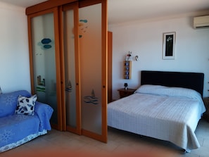 A bedroom with a bed, a sofa, a wardrobe, a nightstand, and a wall-mounted shelf. - Luxury Apartment with superb sea views, mountain views and terrace (Villefranche-Sur-Mer)