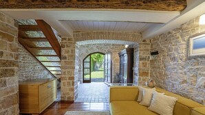 Ein Zimmer mit Steinwänden, einer Holztreppe, einem gelben Sofa und einem Holzkabinett.