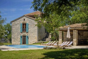 A stone building with a swimming pool and lounge chairs.