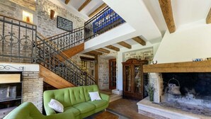 Ein geräumiger Wohnbereich mit einem grünen Sofa, einem Kamin, einer Steinwand und einer Holztreppe.