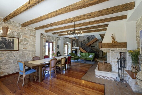 A spacious dining area with a wooden table and chairs, a stone wall, and a staircase leading to an upper level.