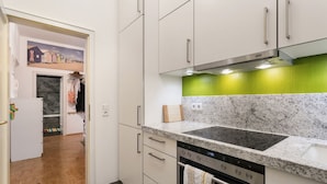 A modern kitchen with white cabinets, a granite countertop, a built-in oven, and a green backsplash. - Family-friendly 3-room apartment in the middle of hip Pieschen (Dresden)