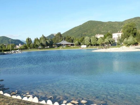 Un lac aux eaux limpides, bordé d’une rive rocheuse et entouré de verdure et de bâtiments.
