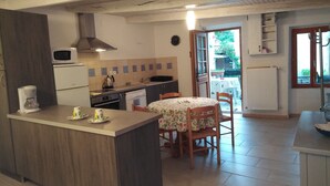 Una cocina con una isla central, una mesa de comedor con sillas, microondas, cafetera y vistas al exterior por una puerta.