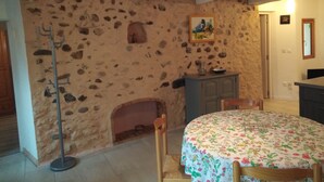 Una habitación rústica con pared de piedra, chimenea, una mesa redonda con mantel floral y una silla de madera.