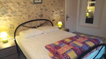 A bedroom with a stone wall, a bed with a colorful quilt, two bedside lamps, and a door with a mirror.