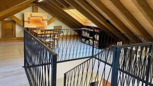 An attic room with a wooden ceiling, a staircase, and a bookshelf.