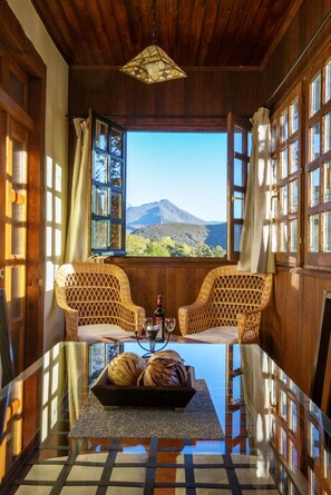 A room with a wooden ceiling, two wicker chairs, a table with a tray of bread, and a view of mountains through a window. - Rural apartments in full nature (Cangas del Narcea)