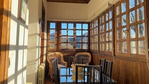 A dining area with a wooden ceiling, large windows, wicker chairs, a glass-top table, and a radiator.
