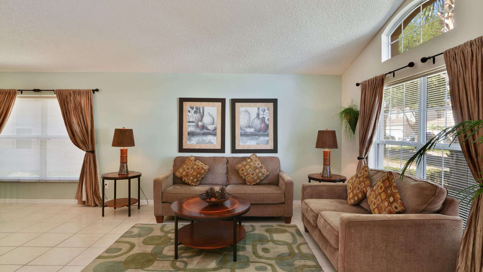 Un salon comprenant deux canapés, une table basse et deux tables d’appoint avec des lampes. Deux tableaux encadrés ornent le mur, et la pièce est dotée d’une grande fenêtre avec des rideaux.