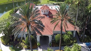 A large house with a red-tiled roof, surrounded by palm trees and a body of water. - Popular 4 bedroom pool home is a must for family fun, located in Emerald Island (Kissimmee)