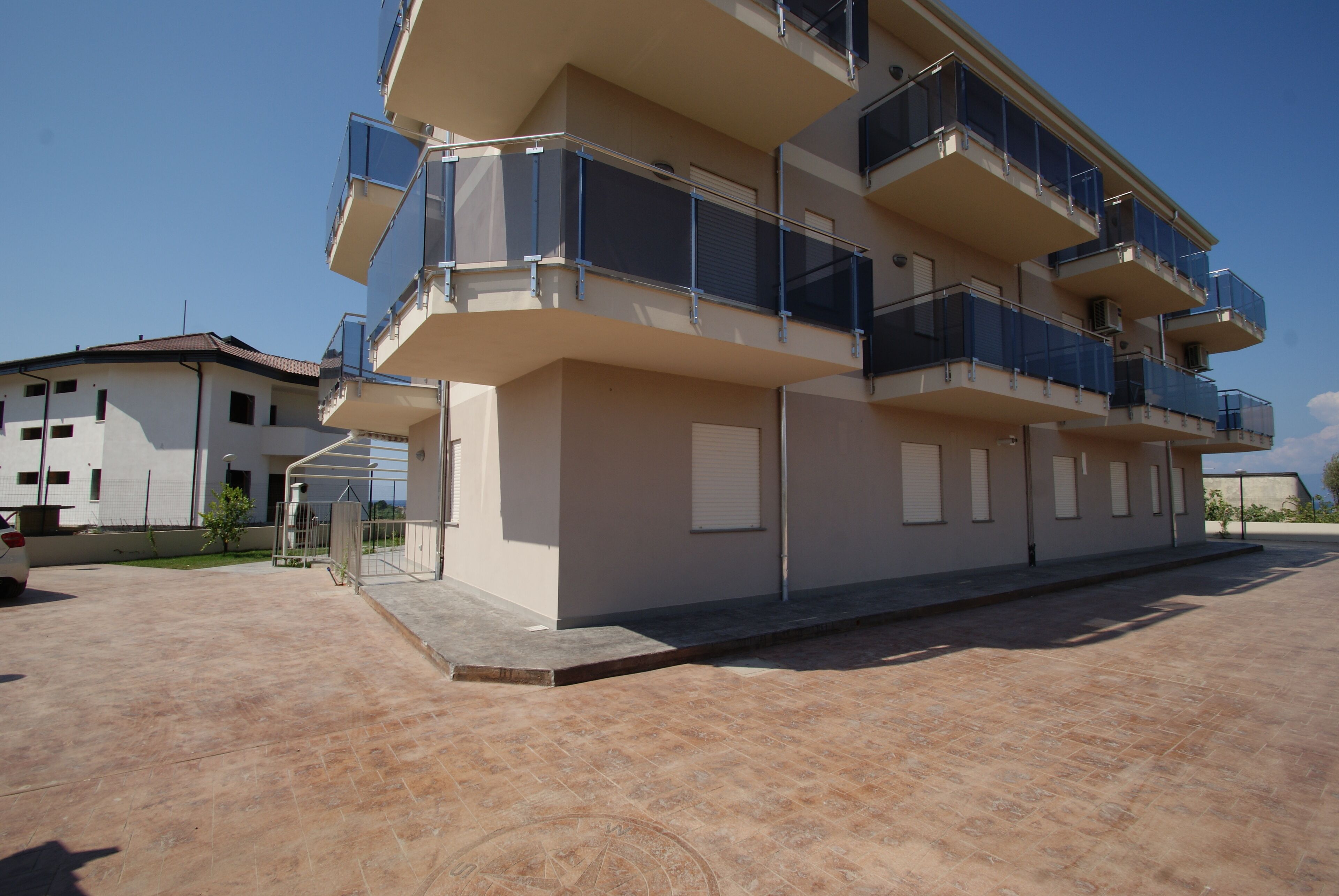 A multi-story residential building with balconies, a paved driveway, and a clear sky.