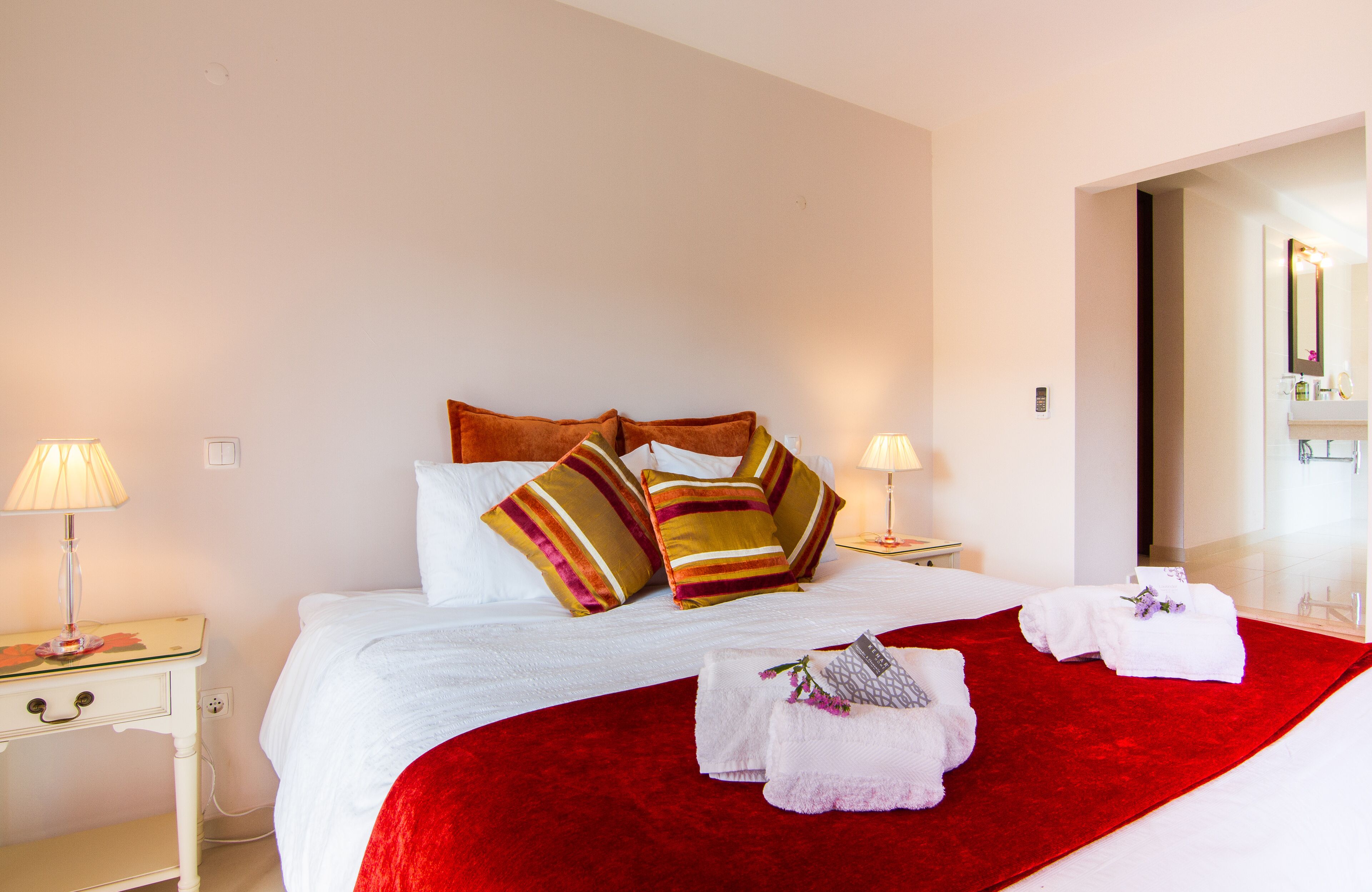 Une chambre d’hôtel avec un grand lit, un plaid rouge, des oreillers blancs et deux lampes de chevet.