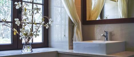A bathroom with a window, a vase with flowers, a sink, and a mirror.