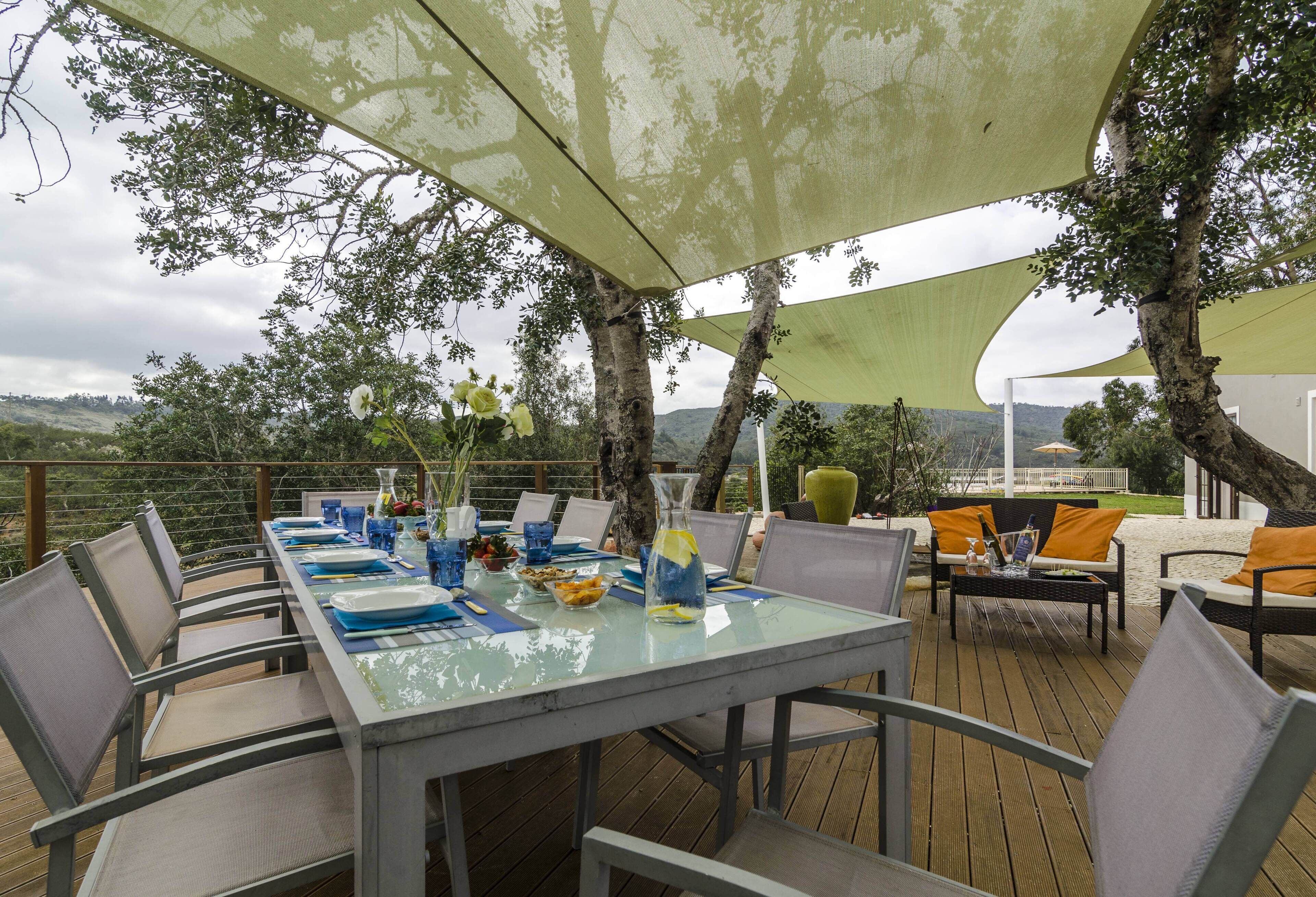 An outdoor dining area with a table set for four, surrounded by chairs, under a shaded canopy.