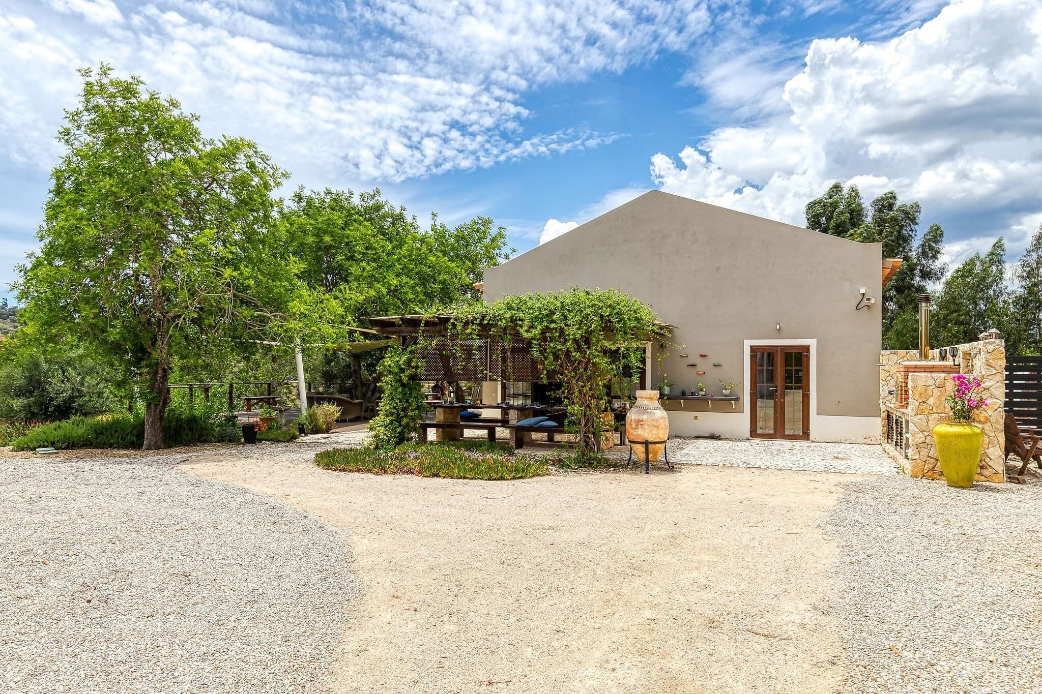 Een gebouw met een strak, modern ontwerp, een grindpad en een kleine tuin met een pergola en plantenpotten.