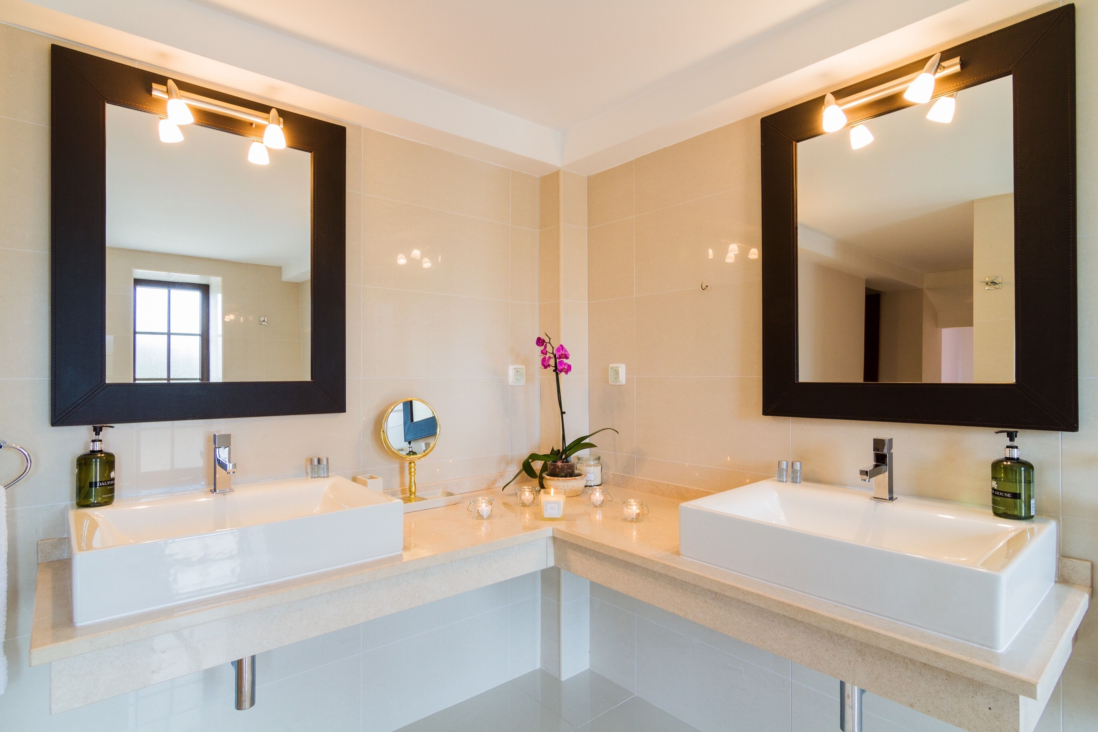Ein modernes Badezimmer mit zwei Waschbecken, großen Spiegeln und einem Fenster.