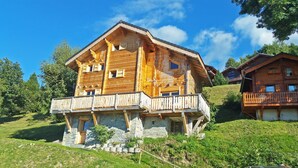 Una cabaña de madera con base de piedra, varios balcones y una vista panorámica de la ladera.
