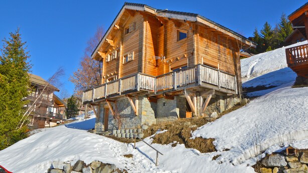 Una cabaña de madera con balcón, ubicada en una ladera cubierta de nieve.