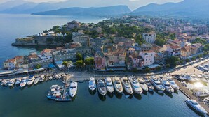An aerial view of a coastal town with historic buildings, a marina with yachts, and a prominent fort on a cliff overlooking the sea.