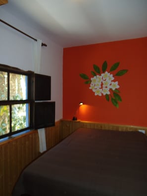 Ein Zimmer mit Bett, Fenster mit Jalousien, einem an der Wand befestigten Fernseher und einer Lampe.