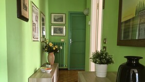 A hallway with green walls, a wooden floor, a reception desk with a vase of flowers, and framed pictures on the wall. - Apartment - Bellagio House of the Sun (Bellagio)