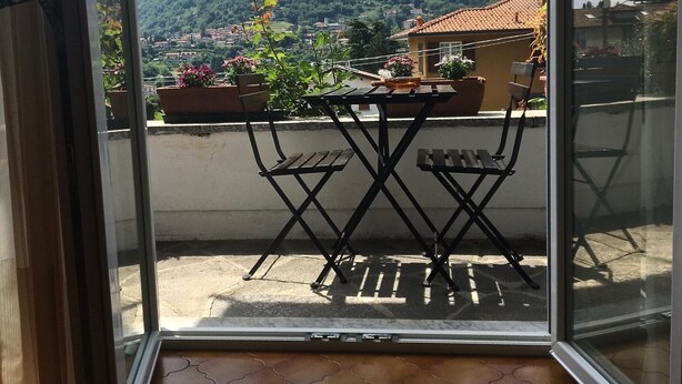 A balcony with a table and chairs, overlooking a mountainous landscape with houses and greenery. - Apartment - Bellagio House of the Sun (Bellagio)