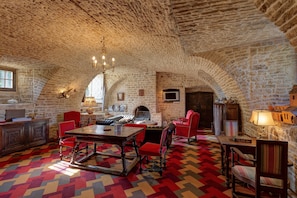 Une pièce avec un plafond en pierre, une cheminée, une table à manger avec des chaises et un tapis coloré.