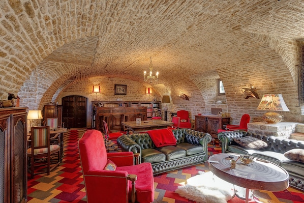 Une pièce chaleureuse aux murs de pierre, avec un canapé en cuir, des fauteuils rouges et un tapis à motifs.
