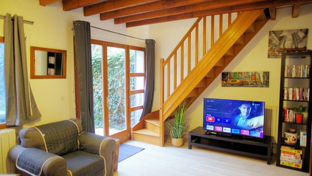 A living room with a sofa, a TV on a stand, a staircase, and a bookshelf.
