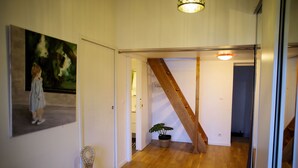 A hallway with wooden flooring, a staircase, a potted plant, and a painting on the wall.