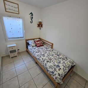 A bedroom with a bed, a window with a view, a wall decoration, and a bedside table. - Villa *** quiet 50m from the beach close to all shops (Mimizan)