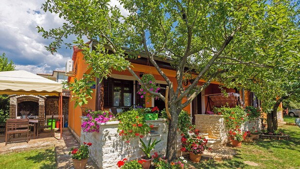 Una casa rústica con fachada de piedra, una mesa y sillas de madera afuera, y plantas en macetas alrededor del jardín.