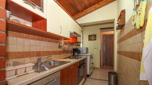 Cocina compacta con lavavajillas, estufa y pileta. Hay un bote de basura y una ventana con cortinas.