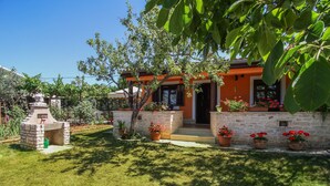 Una casa con fachada de piedra, chimenea de ladrillo y un césped cuidado con plantas en macetas.