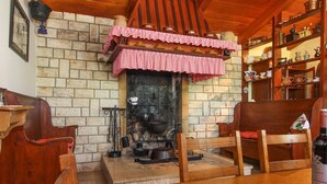Un interior rústico con chimenea de piedra, muebles de madera y una estantería con diversos utensilios de cocina.