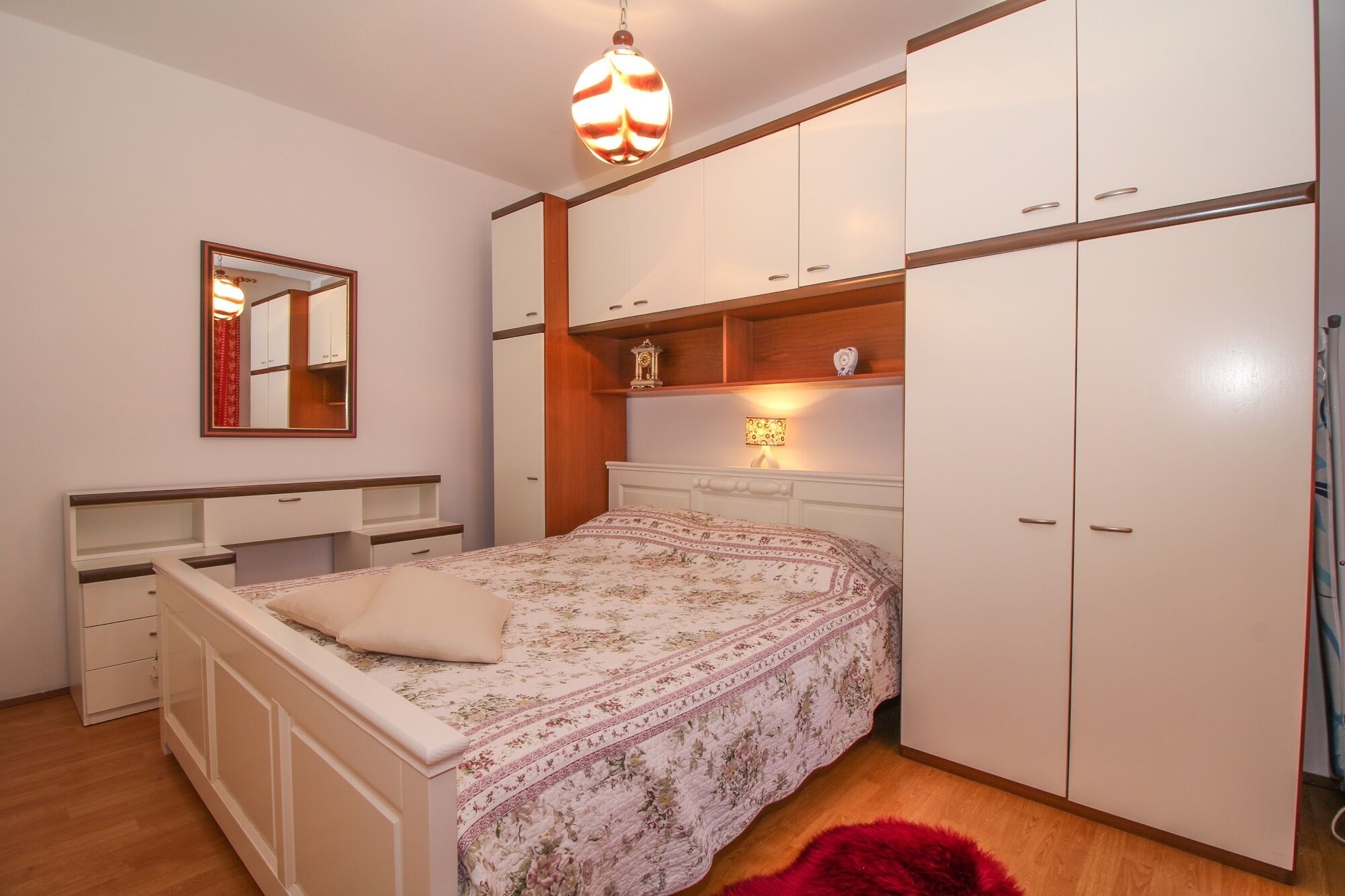 Een slaapkamer met een bed, een kledingkast, een spiegel en een hanglamp.