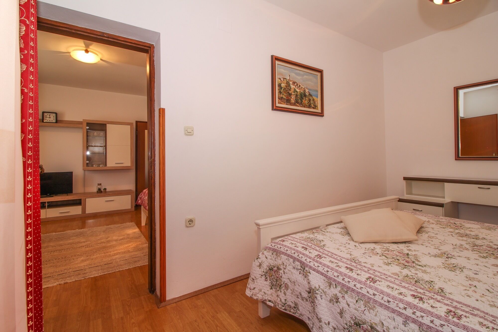 Een slaapkamer met een bed, een kaptafel, een spiegel en een schilderij aan de muur.
